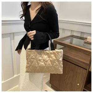Detail view of large beige quilted tote bag with black straps held by elegant female model