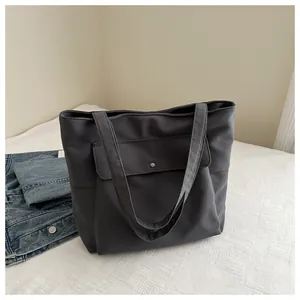 Détail du grand sac cabas gris foncé avec boucle métallique sur un lit de style épuré
