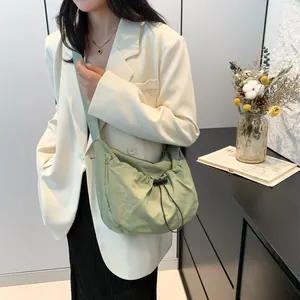Detail view of a pale green ruched crossbody bag featuring adjustable drawstring and wide strap