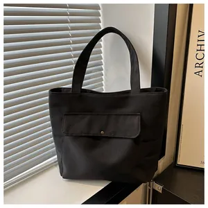 Détail du sac cabas en toile noire montrant la poche avant avec bouton pression et anses solides