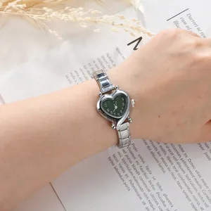 Close-up of heart-shaped silver quartz watch with a vintage green dial on printed background