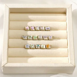 Nahaufnahme vergoldeter modularer Charms mit bunten Herzen und Sternen in einer Schmuckbox