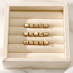 Close-up of golden Italian charm links with enamel, pearls, and crystals on a beige tray