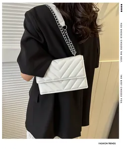 Detail view of a white quilted flap shoulder bag with silver metal chain on black suit