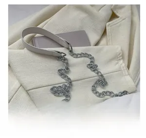 Detail of white quilted crossbody bag featuring a wide leather strap and silver chain