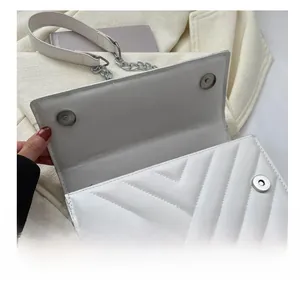Detailed view of the silver magnetic buckle on a white quilted leather bag with V-stitches