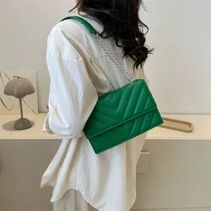 Detail of green quilted crossbody bag with silver chain strap and chevron stitching