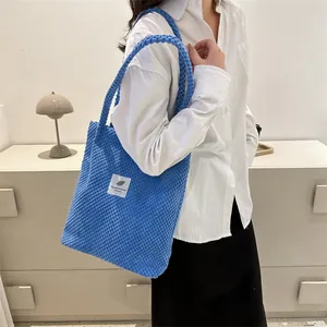 Detail of blue textured tote bag with rope handles and a white square graphic patch