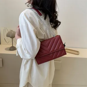 Detail of dark red quilted crossbody bag featuring silver chain strap and V-pattern