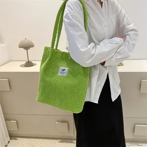 Detail of green corduroy tote bag with white woven label on a model in a minimalist setting