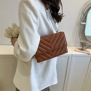 Detailed close-up of brown V-quilted faux leather bag with silver chain strap on model