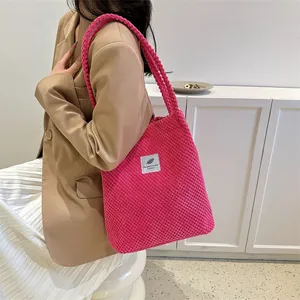Detail of rose pink corduroy tote bag with embroidered label held by a model