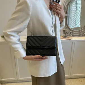 Detail of a black chevron quilted flap bag with silver chain strap on a model
