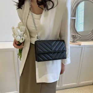 Detail of a chic black quilted crossbody bag with silver chain strap on a white blazer