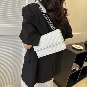 Close-up of white V-quilted crossbody bag with silver chain strap worn by a model