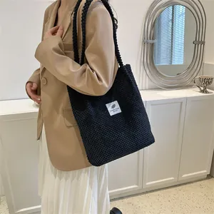 Detailed view of black textured corduroy tote bag with fashion label on shoulder