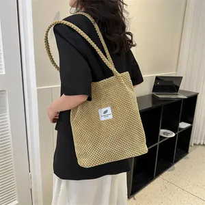 Model wearing a khaki knit tote bag with waffle texture and feathered fabric label