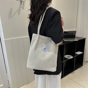 Detail of off-white tote bag with textured waffle fabric and blue feather patch logo