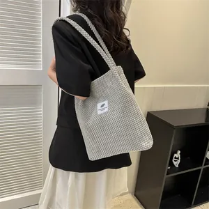 Close-up of light gray knitted tote bag with logo patch on a female shoulder