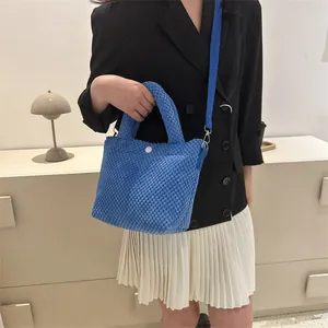 Bolso tipo cubo azul con textura popcorn, asa superior y correa sobre un blazer negro