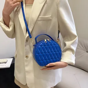 Sac bandoulière rond bleu avec texture géométrique et zips dorés porté par un mannequin
