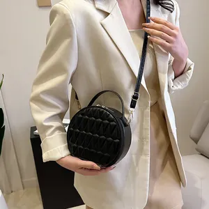 Détail d'un sac bandoulière rond noir avec texture plissée losange sur un blazer blanc