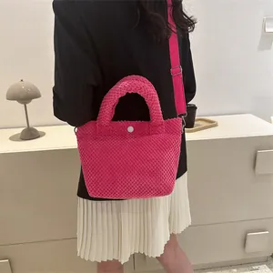 Detalle de bolso cubo fucsia texturizado con botón blanco y correa ajustable