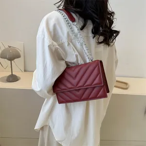 Deep red V-quilted faux leather crossbody bag with silver chain strap worn by model