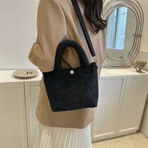 Detalle de bolso tipo cubo negro con textura de gofre, botón blanco y asa ancha