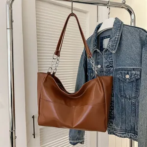 Detail of a large brown tote bag with leather and silver chain handles on a rack