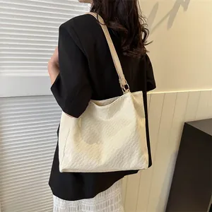 Détail d'un sac cabas beige à texture tissée et bandoulière en cuir porté par un mannequin