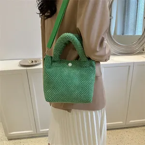 Detalle de textura tejida del bolso cubo verde con botón blanco y correa de hombro
