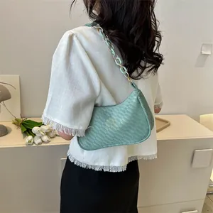 Detail of mint green woven underarm bag featuring a gold chain and acrylic strap on a shoulder