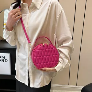 Détail du sac bandoulière rond rouge rose avec texture géométrique et accents dorés