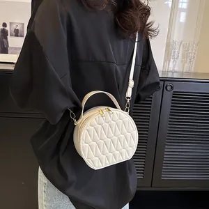 Détail d'un sac bandoulière rond matelassé blanc avec fermetures éclair dorées
