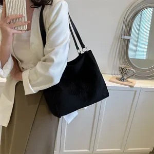 Détail du sac cabas en daim noir montrant le tissu texturé et les fines anses en cuir