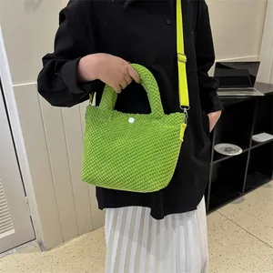 Primer plano de bolso cubo verde brillante con textura, botón blanco y correa ajustable
