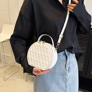 Détail d'un sac bandoulière rond blanc matelassé avec finitions dorées porté par un mannequin