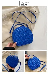 Détail d'un sac bandoulière rond bleu avec texture géométrique et fermeture éclair dorée