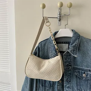 Detail of cream woven underarm bag with unique chain strap against denim jacket