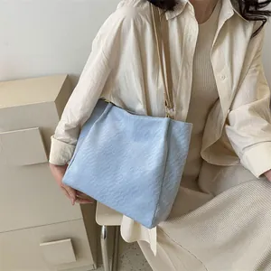 Détail du sac cabas texturé bleu clair avec bandoulière kaki porté par un mannequin chic