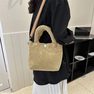 Detalle de bolso tipo cubo de punto beige con correa marrón y herrajes metálicos plata