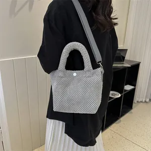 Detalle de bolso gris con textura de burbuja, cierre de presión y correa tejida suave