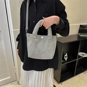 Detalle de bolso tipo cubo gris de textura suave con correa y cierre a presión