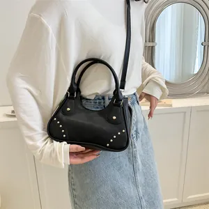 Dettaglio della borsa a mezzaluna in pelle nera con rivetti dorati e manici chic