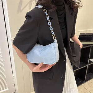 Light blue textured underarm bag with gold and resin chain strap worn by a model