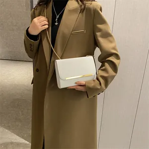 Détail d'un sac à bandoulière en cuir blanc avec barre métallique dorée et bandoulière chaîne