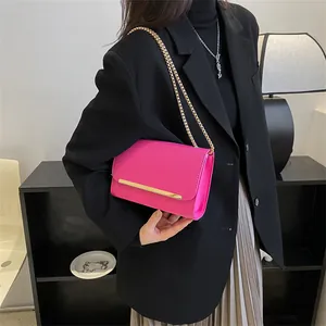 Détail du sac bandoulière rose fuchsia à chaîne dorée porté sur un costume sombre