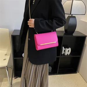Détail d'un petit sac bandoulière fuchsia avec chaîne dorée porté sur un blazer noir