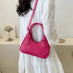 Dettaglio di una borsa in pelle rosso rosa con borchie dorate e tracolla abbinata
